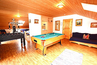 Spiel und Fitnessraum mit Billardtisch, Kicker, Kraftstation und Sitzmöglichkeiten durch Sofa.